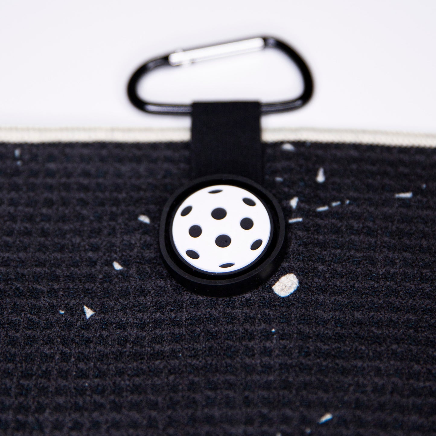 A close-up of a black textured Bodhi Performance pouch with a white zipper, mini pickleball keychain, and black carabiner—perfect for carrying your Performance Pickleball Towel or other Bodhi Performance accessories.