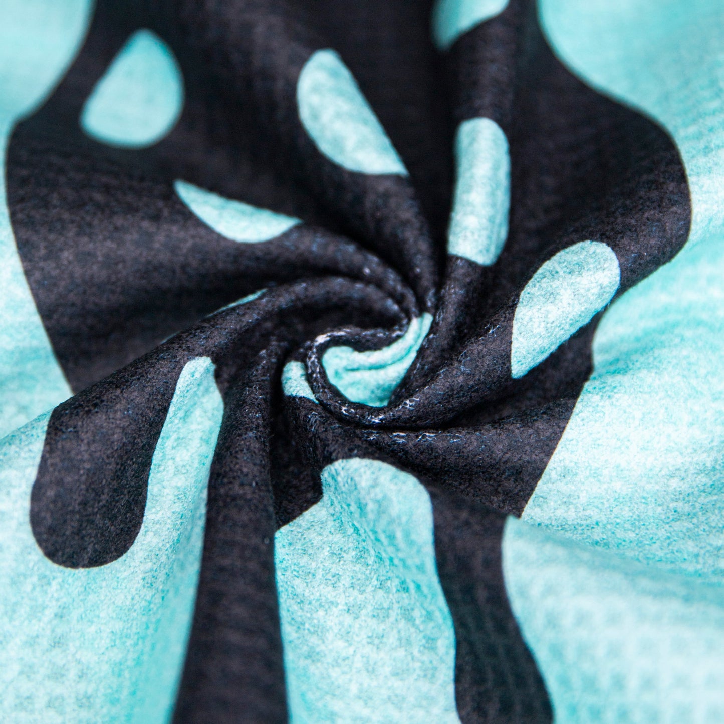 Close-up of the Bodhi Performance Pickleball Towel in turquoise microfiber with black abstract shapes. Twisted in a spiral, its soft folds and bold contrast add motion and style—an ideal accessory from Bodhi Performance.