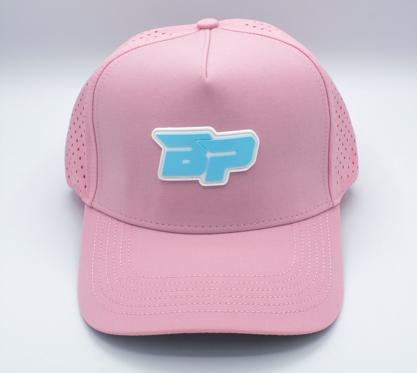 The ICON Snapback by Bodhi Performance is a pink performance pickleball hat featuring a blue and white BP logo on the front, perforated sides, visible stitching on the curved brim, and is displayed against a plain white background.
