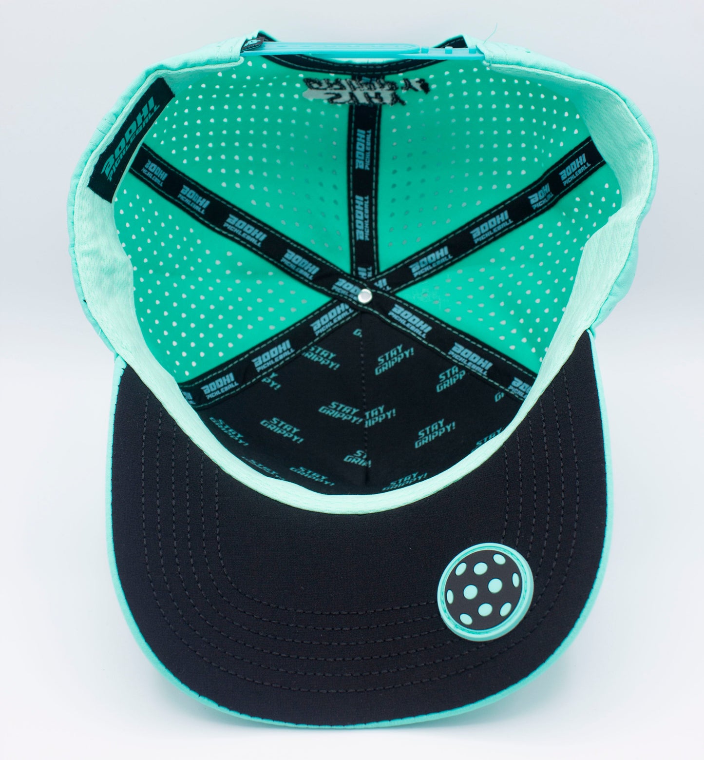 The image shows the inside of a Bodhi Performance ICON Snapback, featuring black fabric strips with repeated white “STAY BAD” text, ventilation holes, and a black under brim with turquoise stitching and a round sticker.