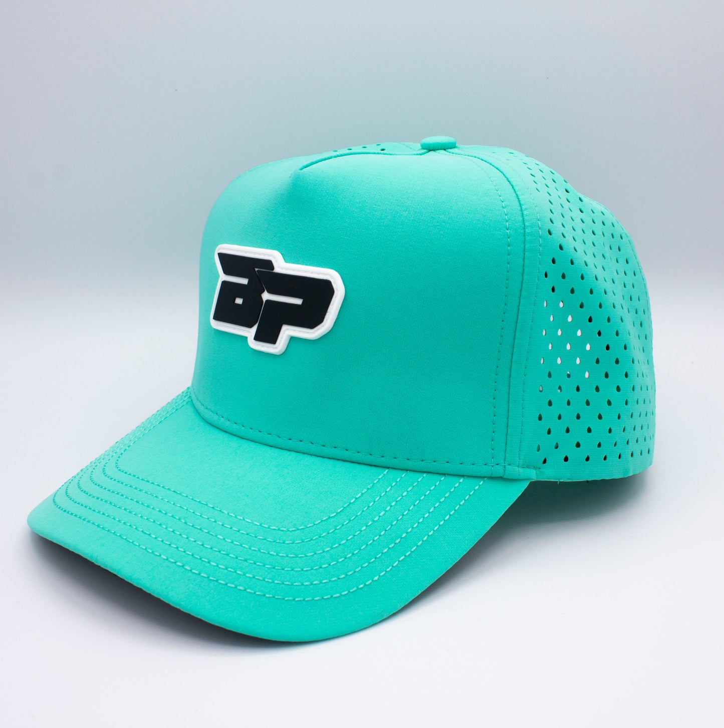 The Bodhi Performance ICON Snapback is a turquoise pickleball hat with a curved brim, perforated side panels, and a bold raised BP logo in black and white on the front. It rests on a light grey surface against a pale background.