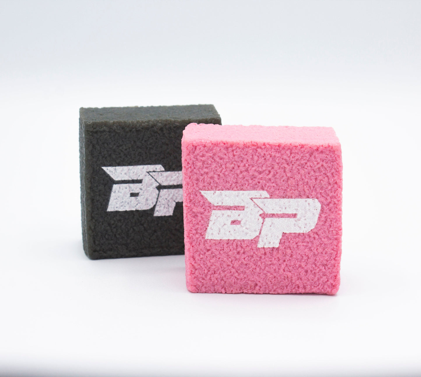 Two pink and black PROeraser™ blocks by Bodhi Performance stand upright on a white surface. Designed for cleaning pickleball paddles, each features a textured finish and a bold white "BP" logo, casting soft shadows on the background.