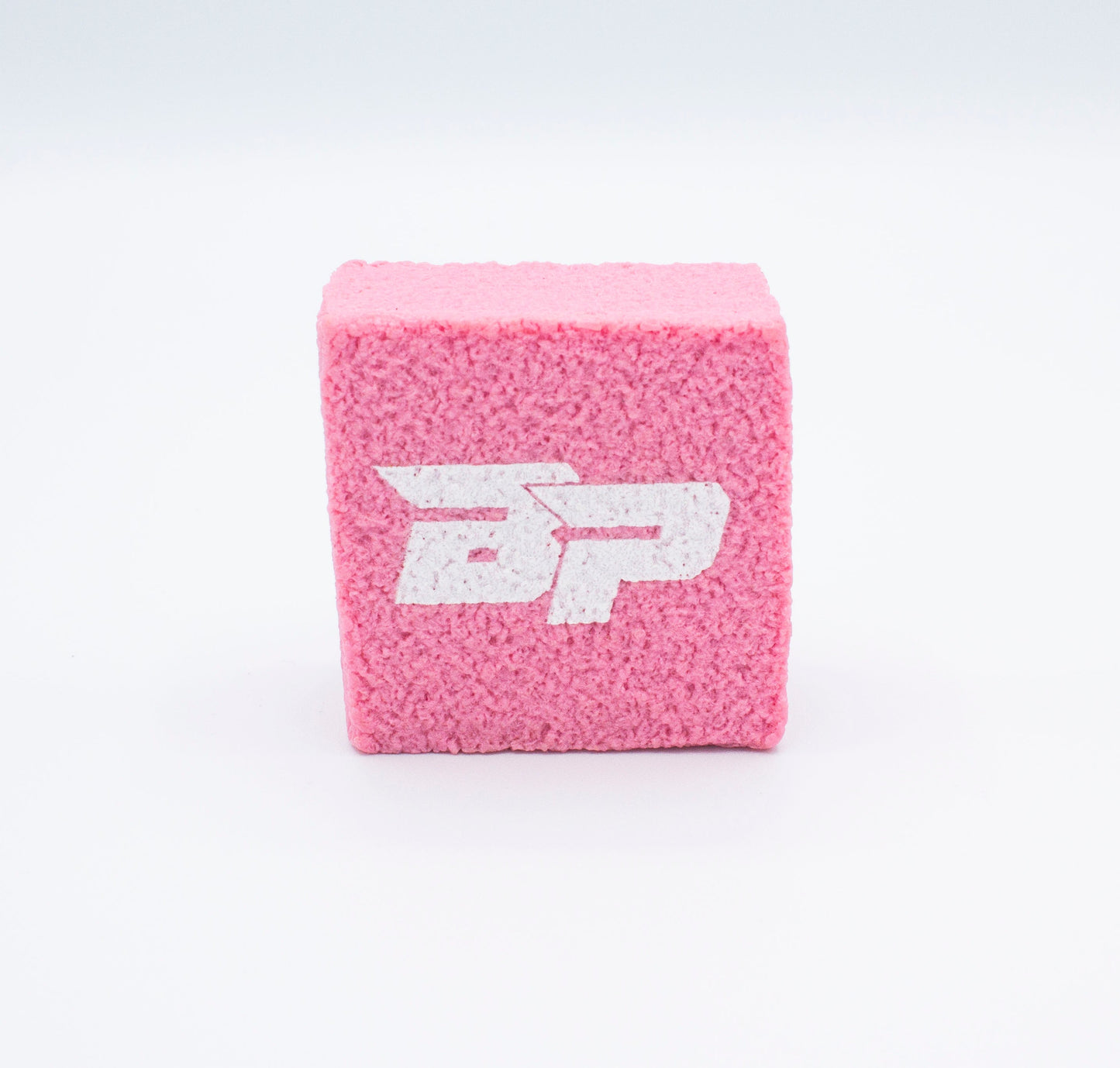 A pink textured cube, the PROeraser™ by Bodhi Performance, stands upright on a white background. Its front displays bold white “BP” letters in a stylized font, resembling a paddle cleaner. The image is evenly lit with no other objects present.
