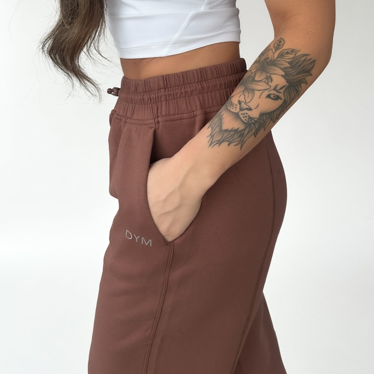 Wearing DYM Athletics' Relax Wide Leg Sweatpant w/ Cinch Drawstring in brown, paired with a white crop top, this cozy loungewear look stands out against a white background. The sweatpants feature high-waist and DYM branding on the side.