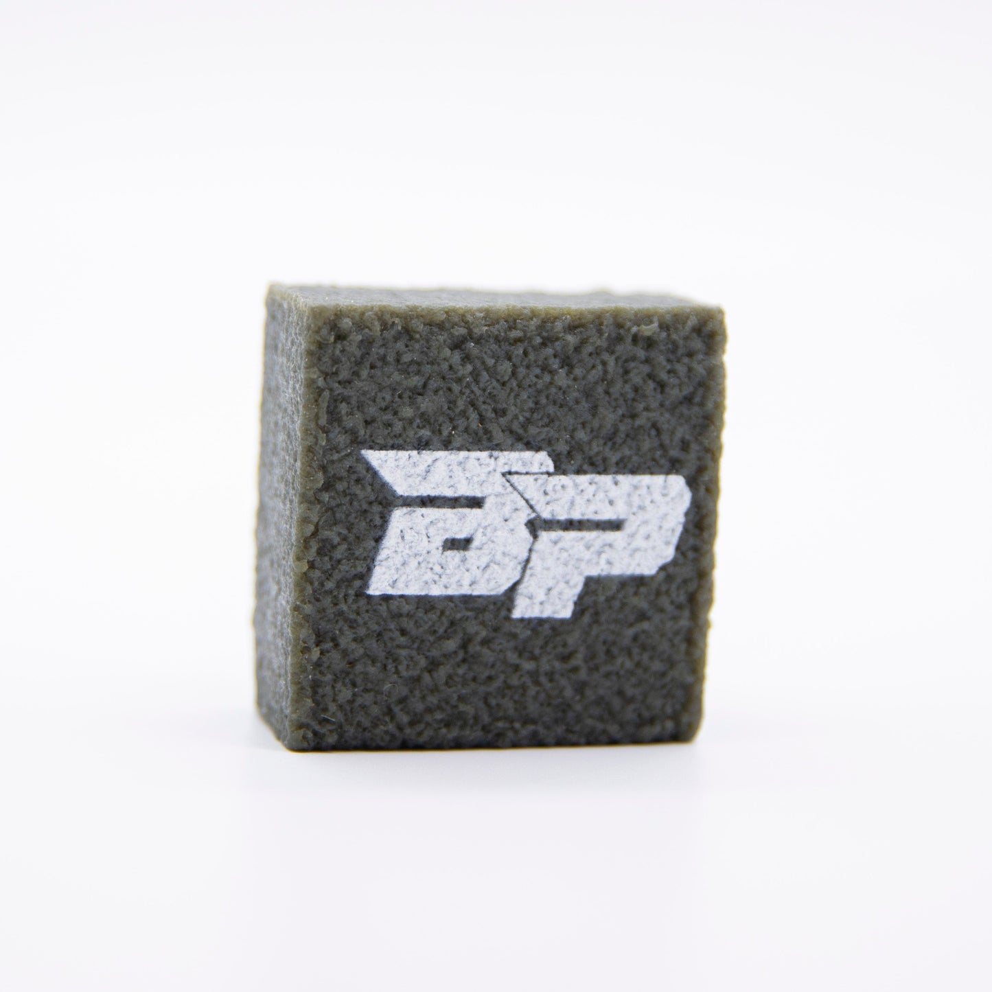 A textured, dark gray cube rests on a white background, featuring a sharp white "BP" logo. Its design echoes the modern, industrial look of the PROeraser™ pickleball paddle cleaner by Bodhi Performance.