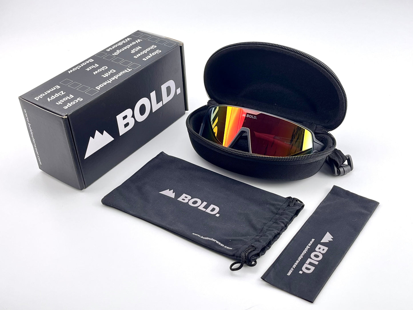 The BOLD Shadows Performance Sunglasses by boldouterwear, featuring red reflective lenses, are displayed in an open black zippered case with a BOLD-branded box, drawstring pouch, and lens cloth on a white background with bold graphics.