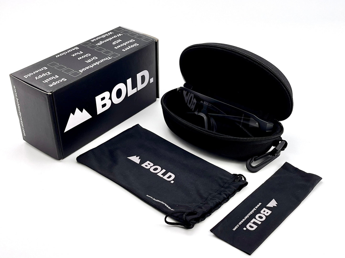 A black boldouterwear box sits next to a black zippered case, drawstring pouch, and cleaning cloth—each branded—on a white background. The case for BOLD Zippy Photochromic Sunglasses – MTB, Ski & Lifestyle Eyewear is partially open, revealing its contents.