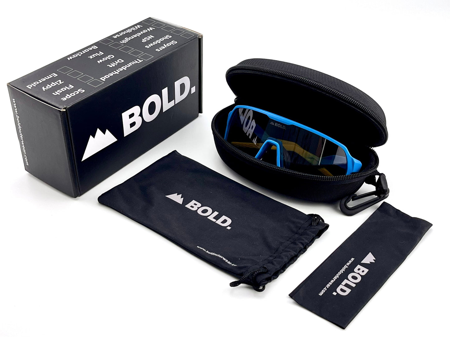 A pair of BOLD Glow Photochromic Sunglasses by boldouterwear with blue frames comes in a black zippered case with carabiner, soft pouch, and lens cloth, all beside a BOLD-branded box listing climb, hike, ski, and bike. Laid on a white surface.