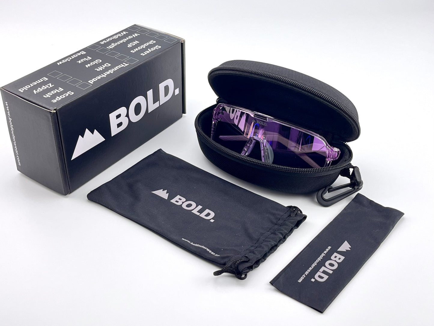 The BOLD Glow Photochromic Sunglasses by boldouterwear, featuring purple lenses, rest in a black zip case. Nearby are a branded cloth pouch and cleaning cloth, with a black BOLD box on the left—all displayed on a white background.