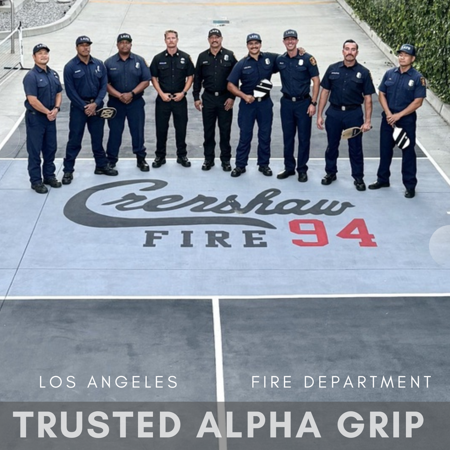 Eight firefighters and a police officer stand on concrete marked with “Crenshaw Fire 94,” painted using SlipDoctors Alpha Grip Non-Slip Stripe and Athletic Court Paint. A text overlay reads “Los Angeles Fire Department Trusted Alpha Grip.” Trees frame the background.