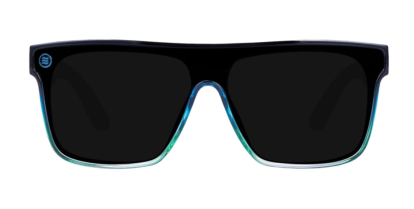 The Turnstile by Neven Eyewear are large, rectangular polarized sunglasses with thick black frames that fade into transparent blue-green. Impact-resistant dark lenses and a small circular logo on the upper left add style and durability.