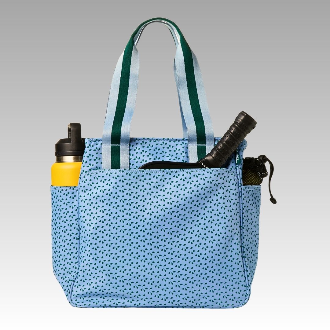 The Lulu Pickleball Tote by Playly Store is a light blue bag with dark blue dots, striped handles, and side pockets—one holding a yellow water bottle, the other a dark item like a yoga mat or accessory.