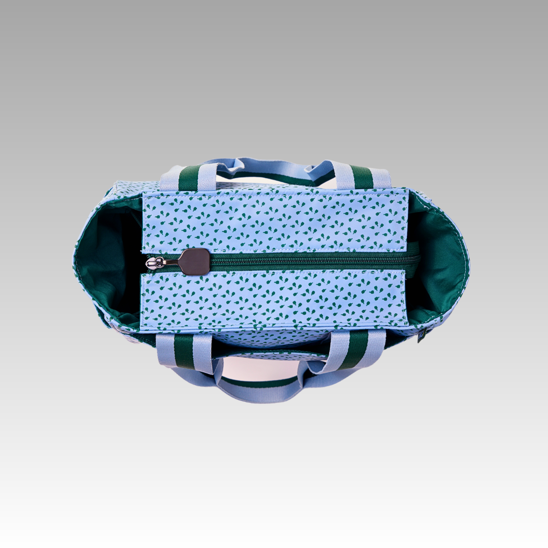 A top-down view shows the Lulu Pickleball Tote by Playly Store, open with a blue exterior featuring green and navy scatter patterns, two striped handles, green interior lining, and a central zippered pocket. The background is gray.