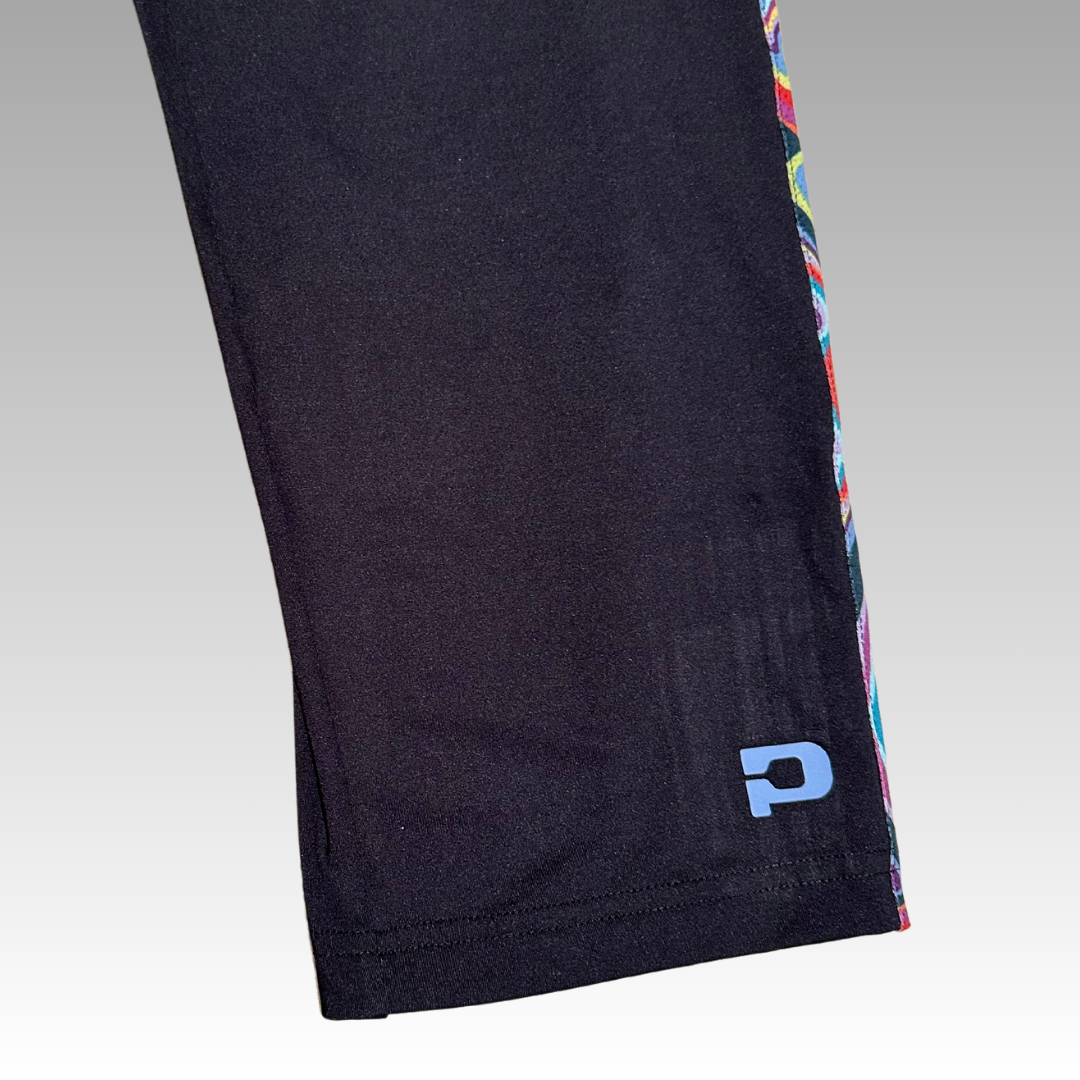Close-up of a Lexi Warm-Up Pant leg by Playly Store in black, featuring a light blue P logo near the hem and patterned side seam. Background fades gray. Made with SwiftForm fabric for comfort and performance.