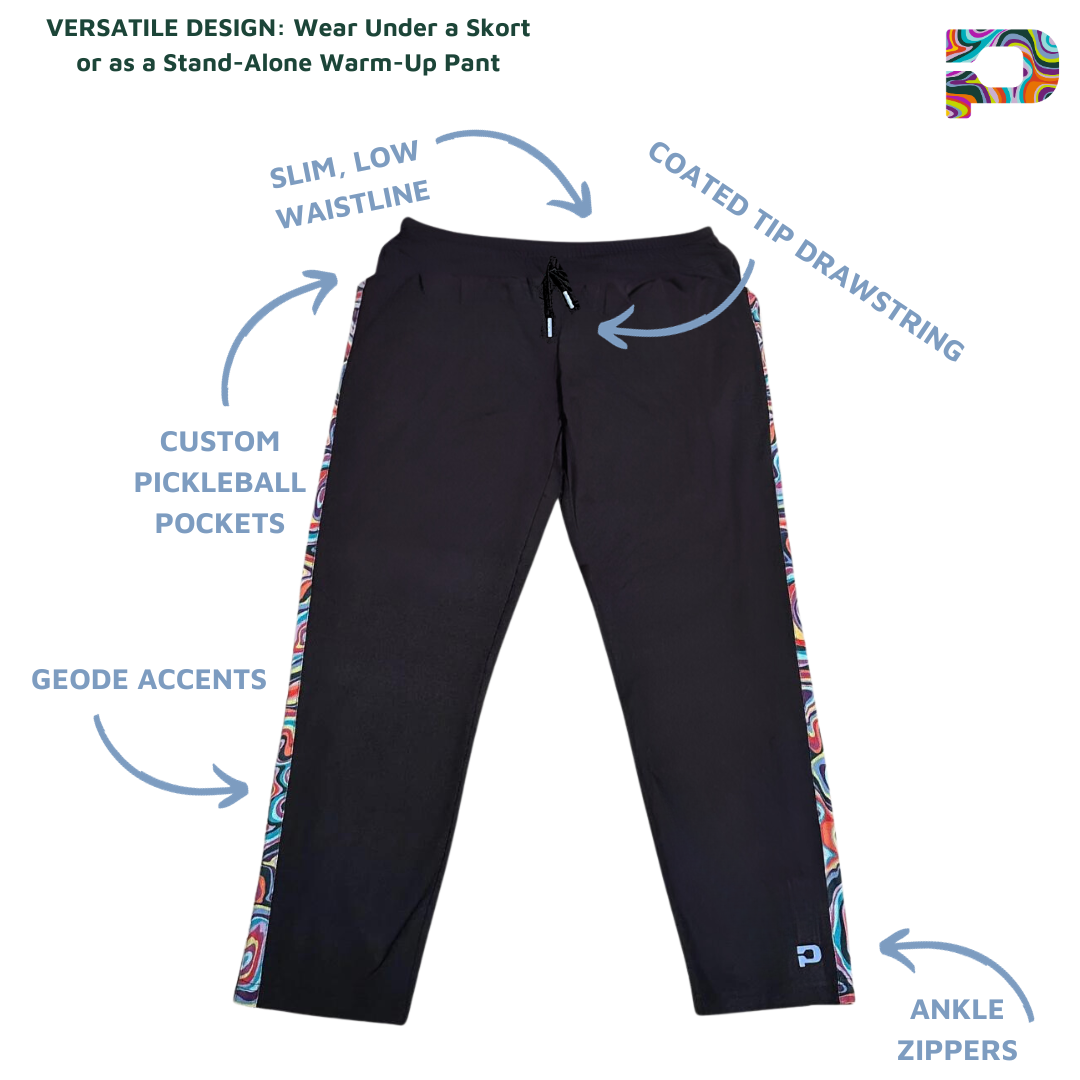 The Lexi Warm-Up Pant by Playly Store is a black athletic pickleball pant with colorful swirl side stripes, made from SwiftForm fabric. Features include a slim low waist, coated-tip drawstring, custom pickleball pockets, geode accents, and ankle zippers.