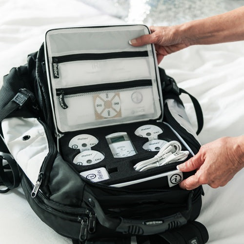 A person opens an iReliev Hard Protective Carry Case for Wireless TENS EMS, revealing a neatly organized kit with labeled round components, a display device, cables, and mesh pockets, all secured in custom foam and zippered compartments.