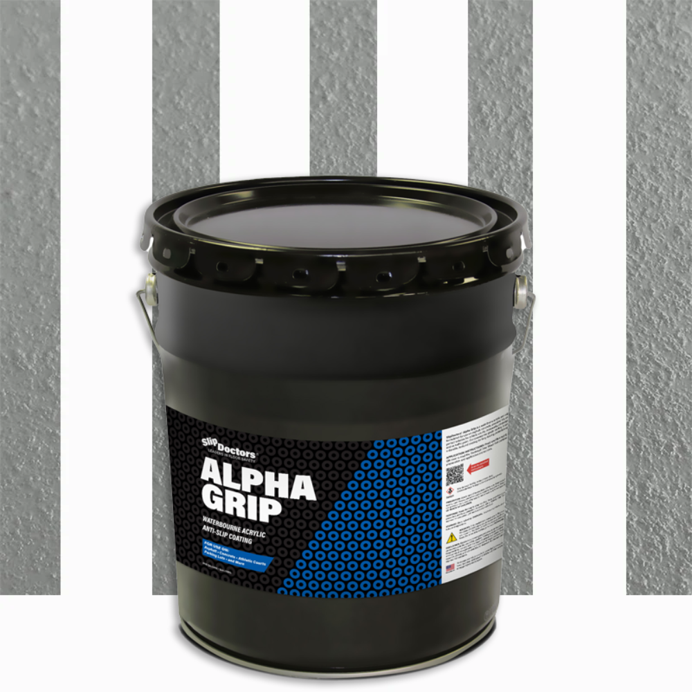 A large black metal pail labeled Alpha Grip Non-Slip Stripe and Athletic Court Paint by SlipDoctors sits in front of a textured gray wall with vertical dark gray stripes. The pail features blue and white geometric details, a metal handle, and a sealed lid.