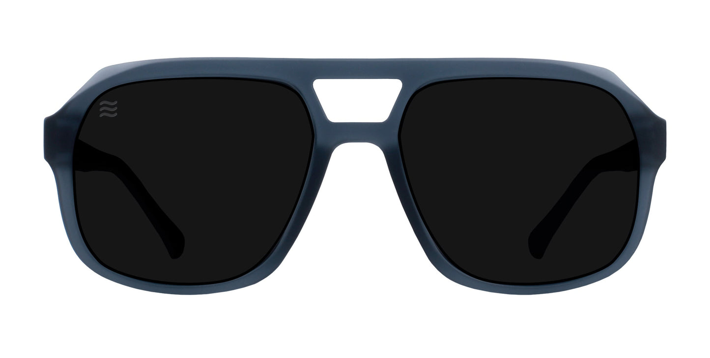 The Koa sunglasses by Neven Eyewear feature matte dark blue-gray aviator frames with a sporty, angular design and thick rims. The large, solid black polarized UV400 lenses have a small wave logo on the left.