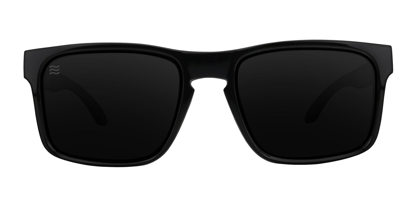 A front view of Neven Eyewear’s Doom XL sunglasses in black shows square, glossy frames with a wave-like logo at the bridge. The thick, curved frame holds dark polarized lenses providing UV protection. Set against a plain white background.