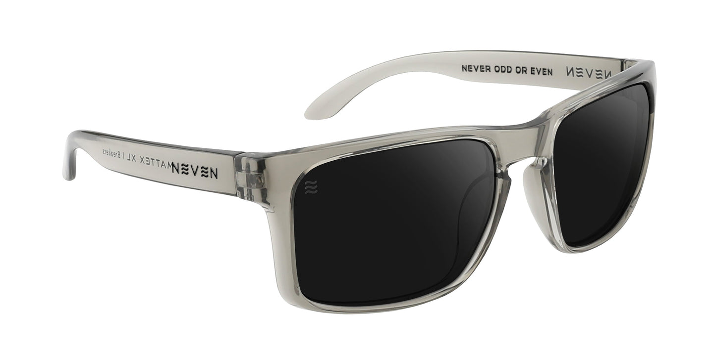 The Breakers XL by Neven Eyewear are rectangular oversized sunglasses with translucent gray plastic frames and black lenses. "NEVER ODD OR EVEN" appears inside the right temple. Shown angled on a white background. Great for large heads.
