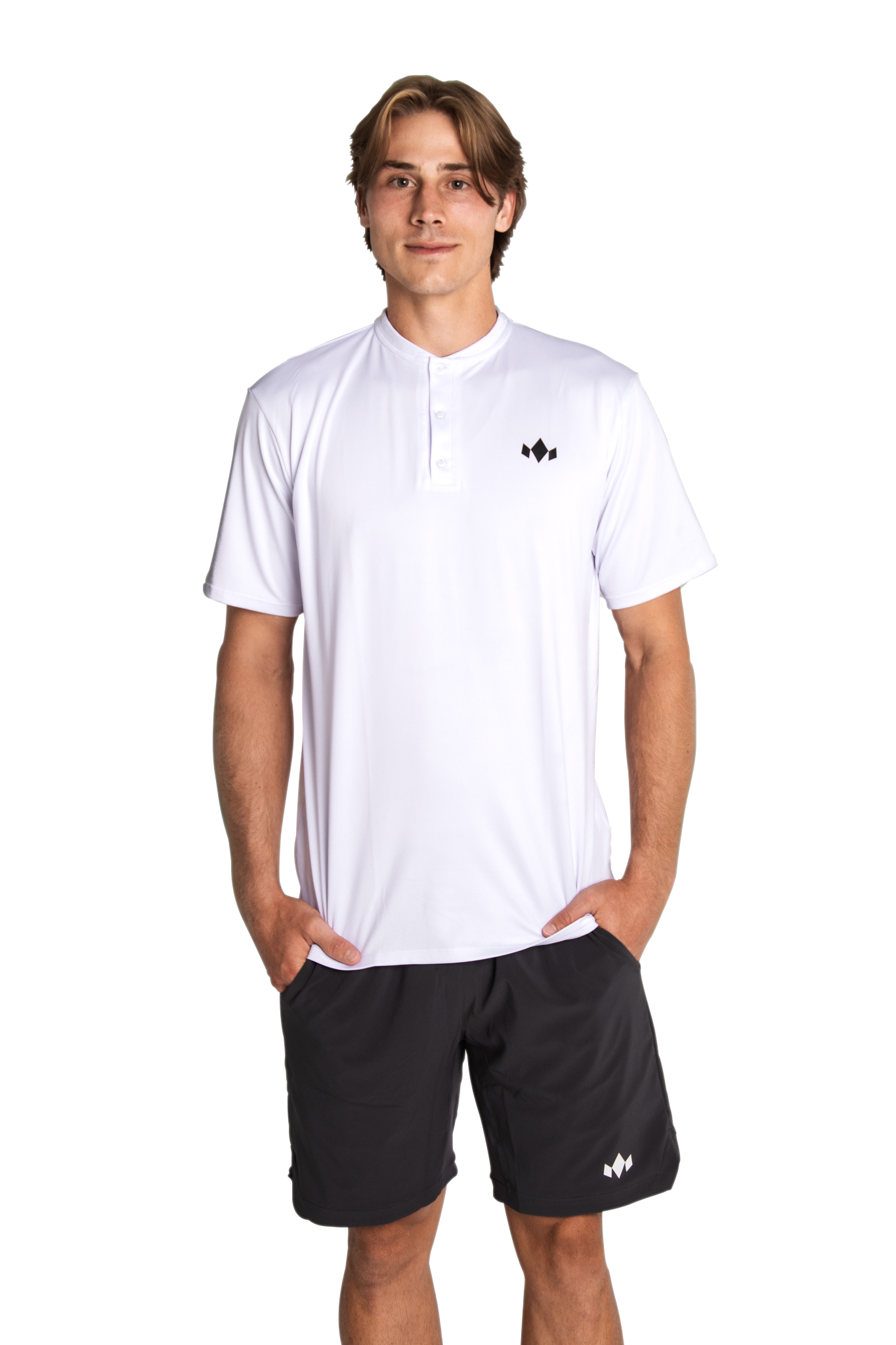 A young man with light brown hair smiles confidently with his hands in his pockets, wearing Diadem Sports Men's Essential Everyday Tops—a white athletic-fit short-sleeve henley shirt with buttons and a small black logo—paired with black shorts.