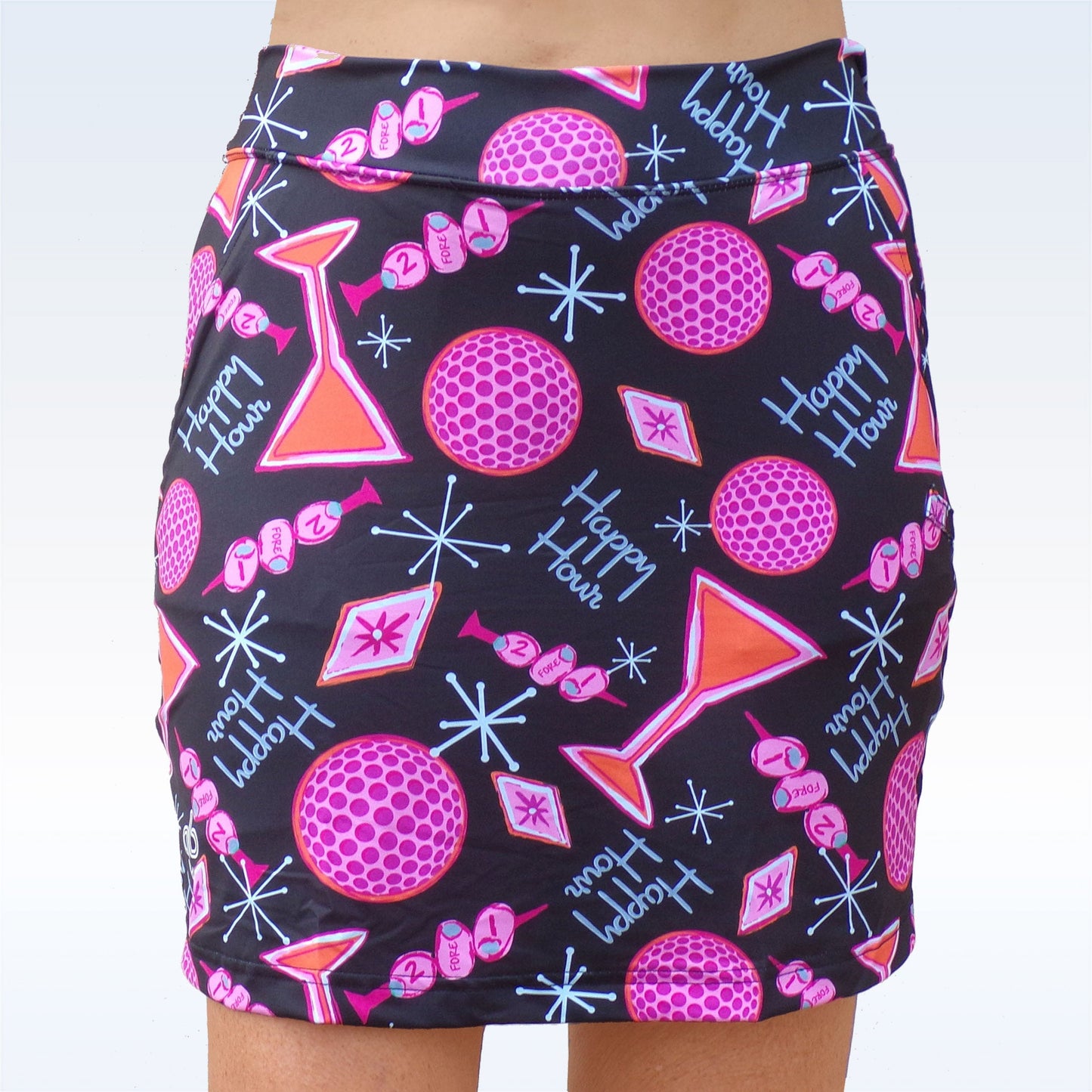 A person wears the Pickleball Bella Martini Straight Golf Skort, a black skort by Pickleball Bella featuring pink martini glasses, cocktail shakers, dice, “Happy Hour” in white, and blue geometric shapes on a light blue background.