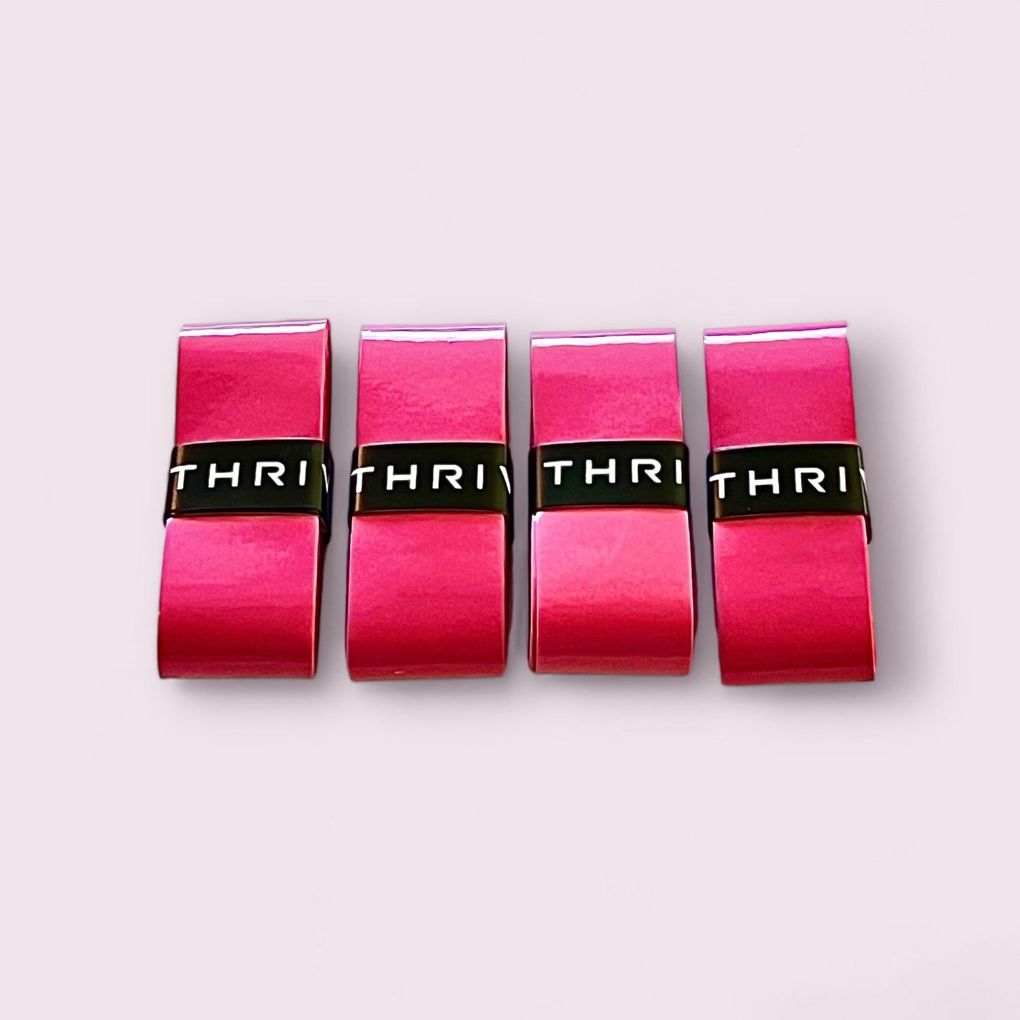 Four bright pink rectangular Thrive Pickleball Overgrips (Super Absorbent) with a glossy finish are arranged side by side on a pale pink background. Each grip features a black band with white letters and offers a comfortable, moisture-absorbing hold.