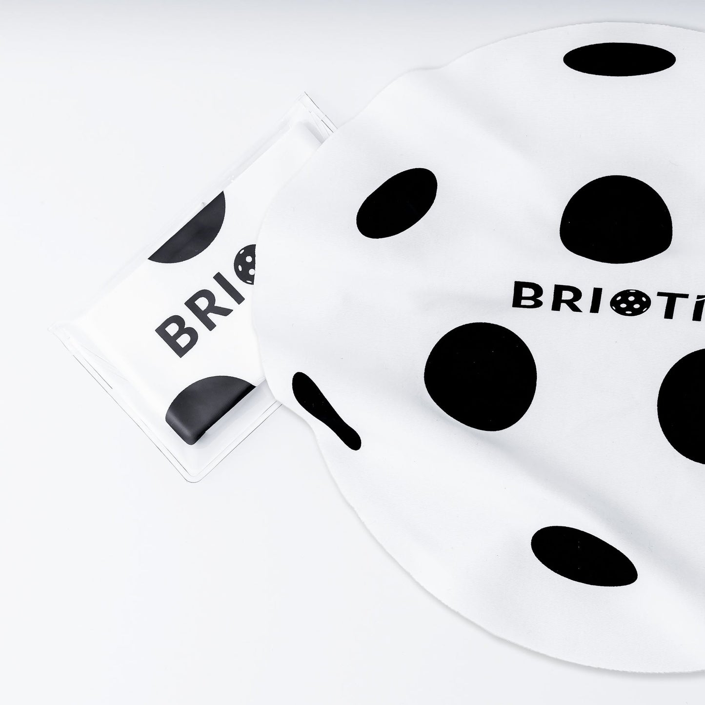 A BRIOTI Lens Cleaning Cloth, known for keeping your gear spotless, is shown next to its polka-dotted packaging. The packaging and the cloth both feature black polka dots and the brand name “BRIOTI” partly visible in black text.