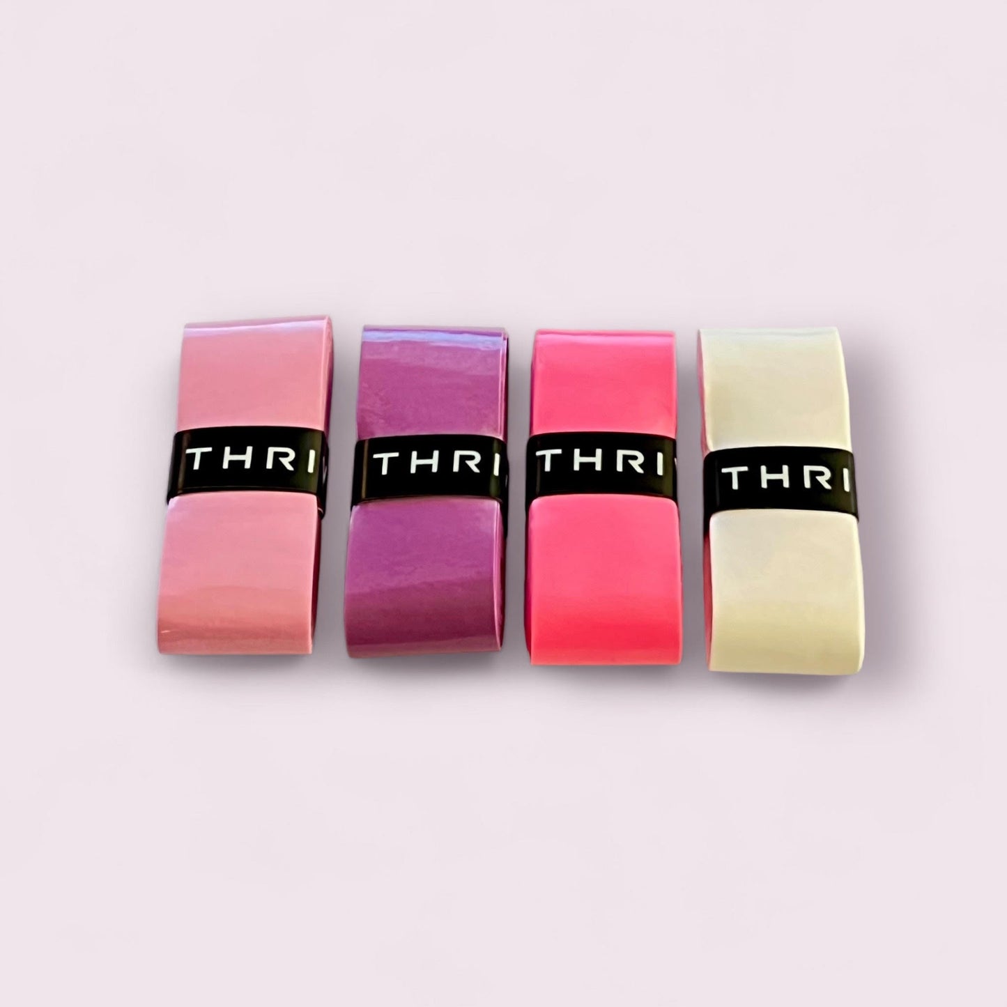Four durable rectangular Overgrips (Super Tacky) by Thrive Pickleball in pink, purple, red, and off-white are arranged side by side. Each grip is wrapped with a black band labeled “THRI” on a light pink background.