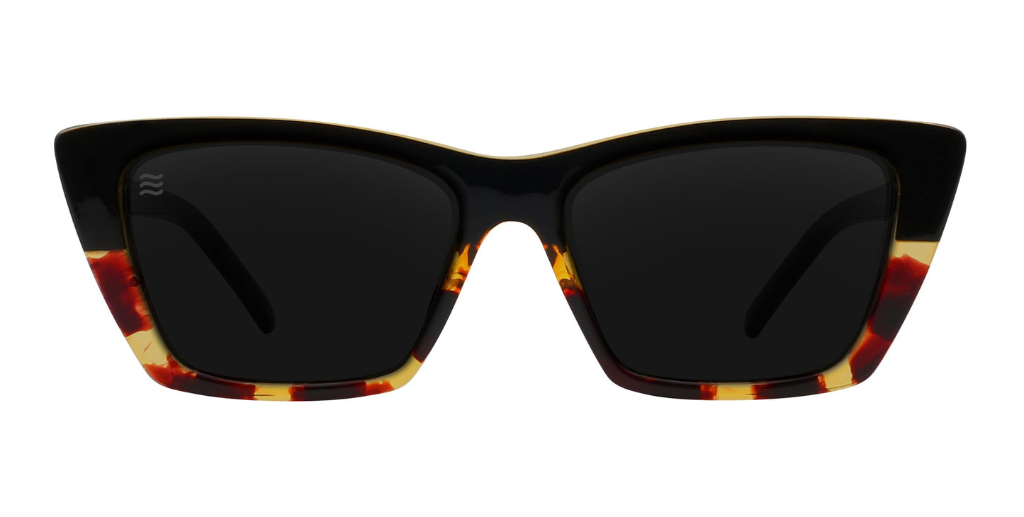 The Neven Eyewear Dusk features rectangular cat-eye frames in glossy black tortoise with dark brown, amber, and yellow accents. Large polarized UV400 lenses and sharply angled edges deliver bold, modern style.