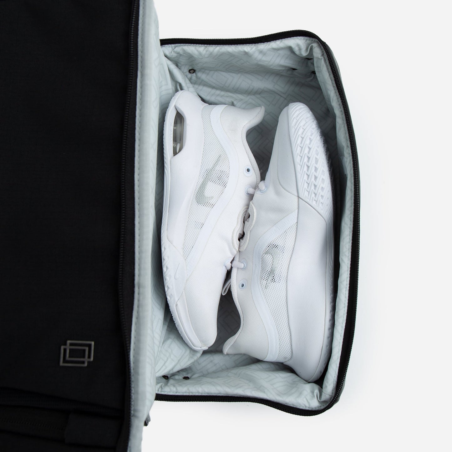 A pair of white athletic shoes with mesh panels are neatly packed side by side in a light gray suitcase, similar to how pickleball gear is organized in the Doubletake NYC Pickleball Backpack. The suitcase is partially unzipped, showing only the shoes and interior.