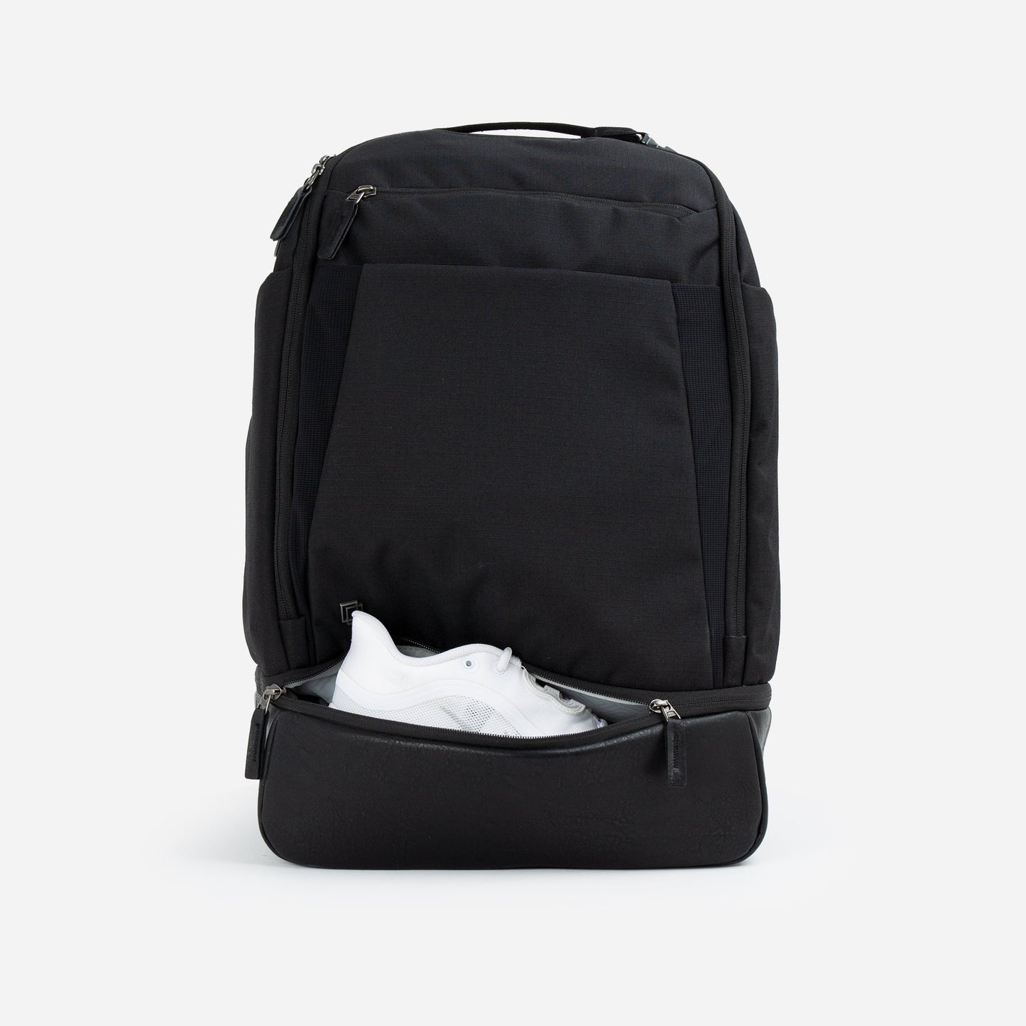 The Doubletake NYC Pickleball Backpack, shown in black on a white background, stands upright with its lower front compartment unzipped to reveal a white sneaker. It features multiple zippered pockets and paddle compartments in a sleek, modern design.