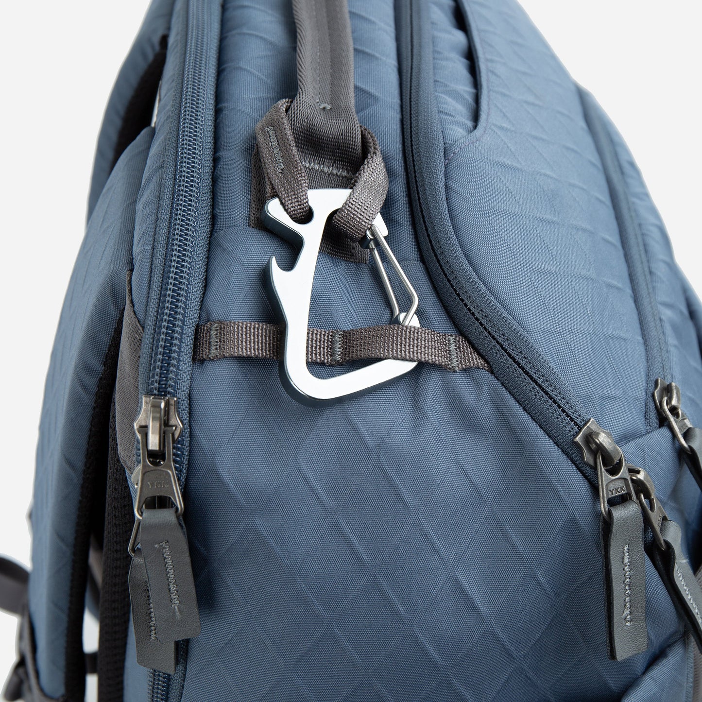 A close-up of the Doubletake NYC Pickleball Backpack shows its blue quilted design, multiple zippered compartments for paddles and gear, a silver carabiner on a gray strap by the zippers, and branded tags. The background is plain and light-colored.