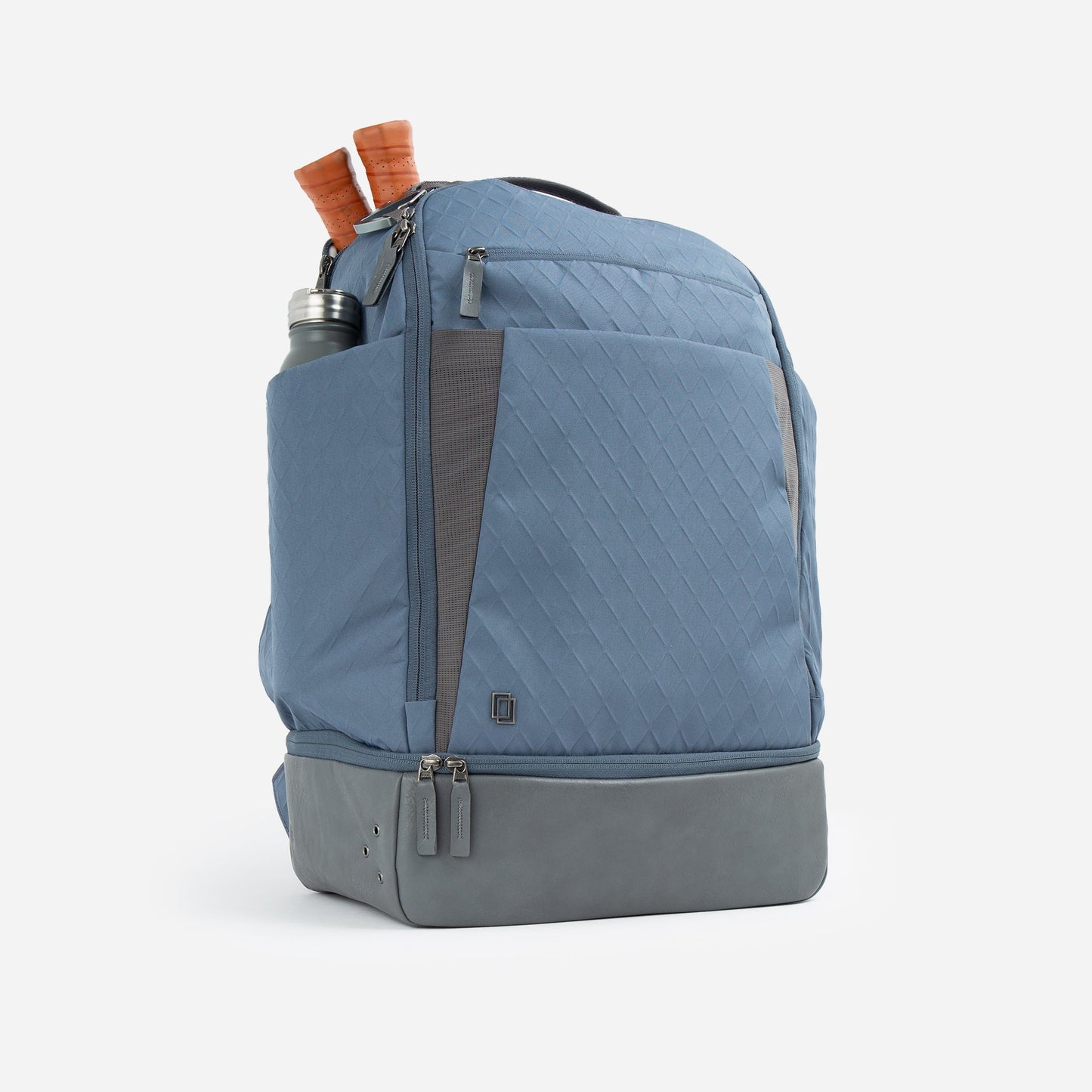 The Doubletake NYC Pickleball Backpack in light blue features a textured diamond pattern, gray base, and side pocket with a metal water bottle. It offers two paddle compartments, multiple zippers, and sits upright against a white background.