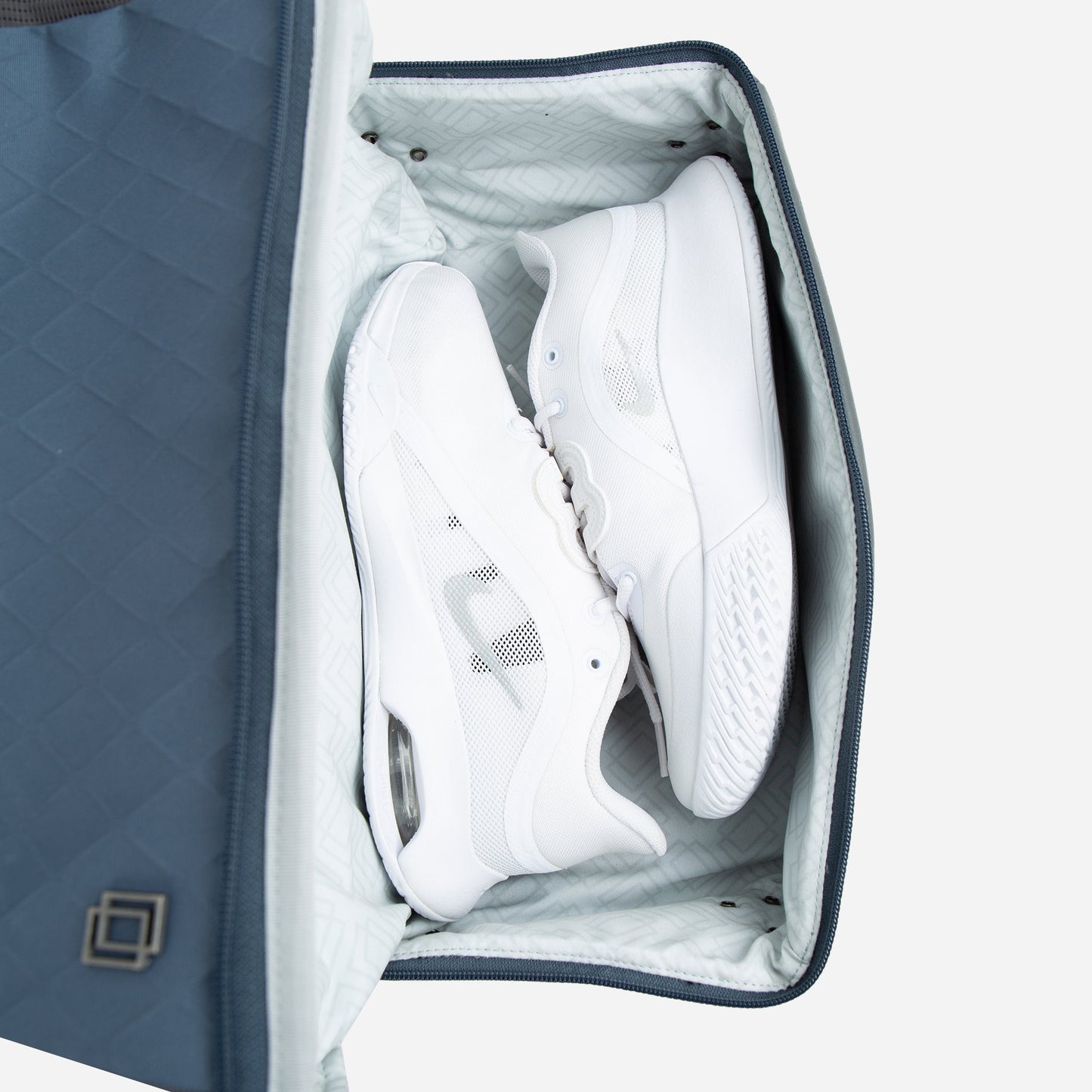 A pair of white athletic sneakers is neatly packed inside the Doubletake NYC Pickleball Backpack, with paddle compartments. The light blue bag is partially open, revealing the shoes side by side against the soft geometric lining.