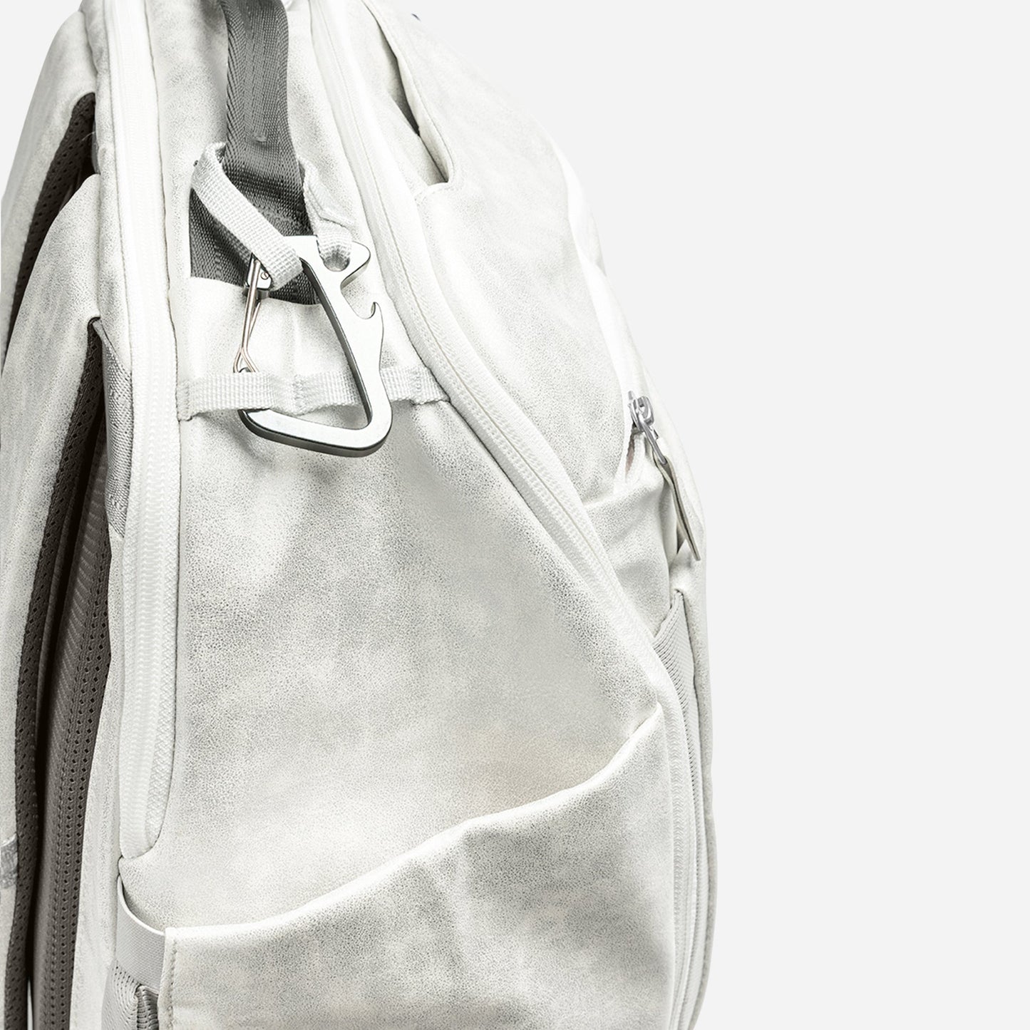 The Doubletake NYC Pickleball Backpack features a white, textured surface with a bold diagonal zipper and a silver carabiner on the top loop. A plain white background showcases the backpack’s stylish design and details.