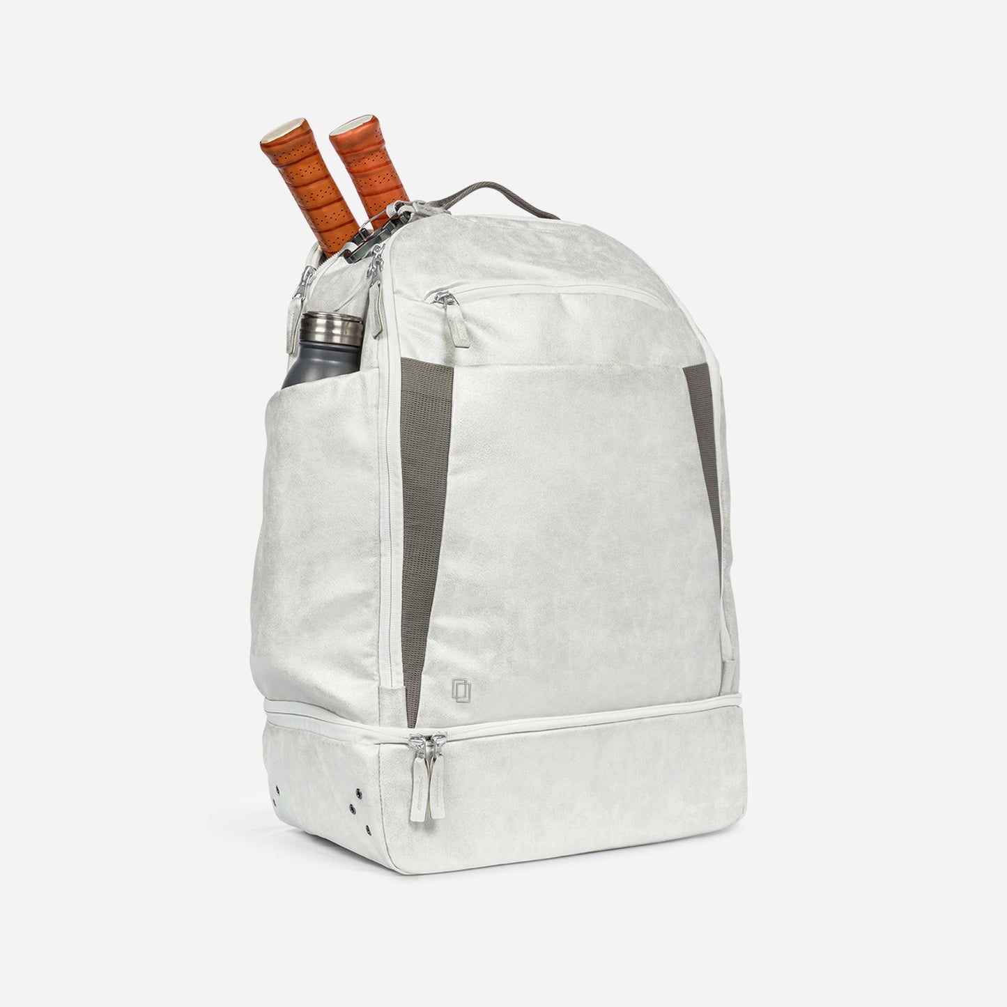 The Doubletake NYC Pickleball Backpack in light gray features a spacious front pocket, side mesh pockets, and a bottom compartment. Two paddles and a stainless steel water bottle are seen sticking out as the backpack stands upright on a white background.