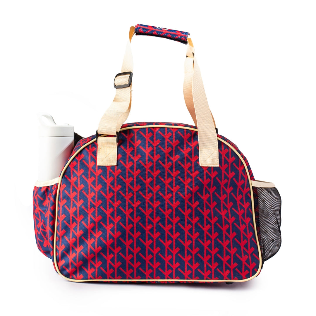 The Court Couture Navy Premium Women's Pickleball Bag by Pik'le'Ball Sports features a red and blue pattern, beige handles and piping, a white bottle side pocket, black mesh pocket, rectangular base, curved top, and is made from sustainable materials.