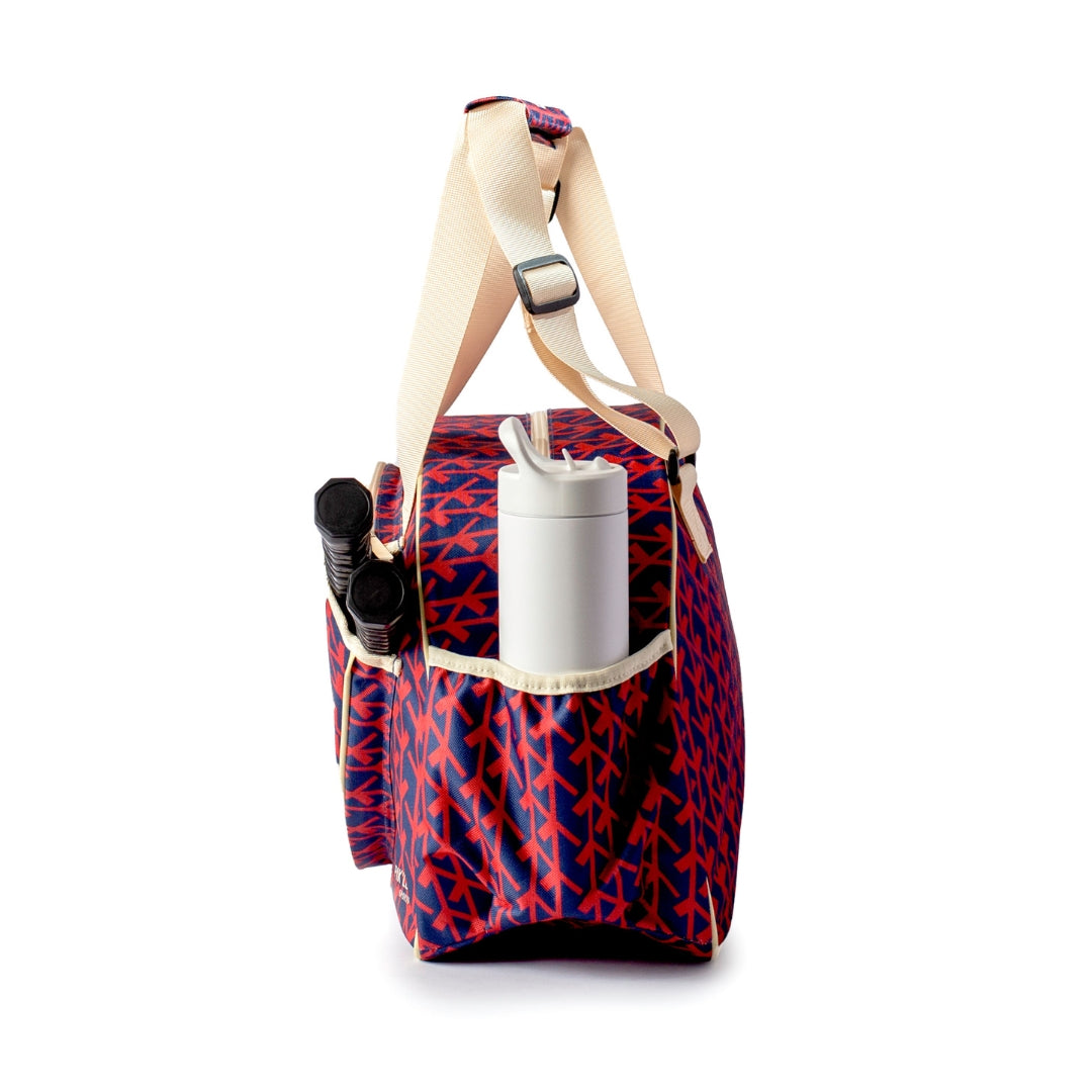 The Pik'le'Ball Sports Court Couture Premium Women's Pickleball Bag features a navy and red geometric pattern, beige woven straps, multiple compartments including a paddle sleeve, and side pocket for a water bottle or umbrella. Background is white.