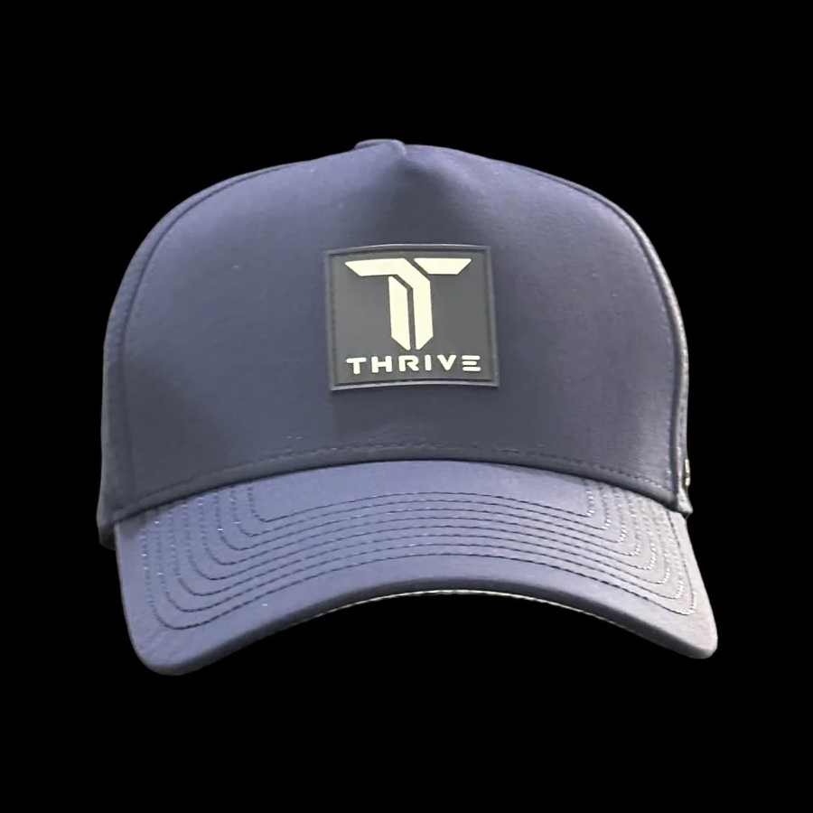 The Thrive Elite Tour Hat by Thrive Pickleball is a navy blue cap featuring a rectangular patch with a bold white “T” and “THRIVE” in uppercase, displayed against a solid black background.