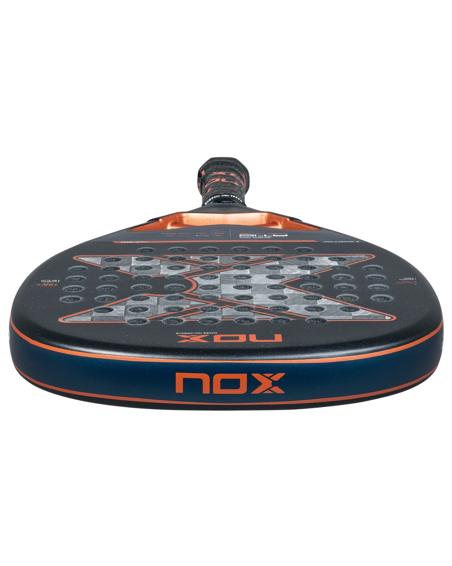 A close-up of the Nox AT10 Luxury GENIUS ATTACK 18K Alum 2025 by Agustin Tapia from Padel USA, showing its round shape, black surface with gray and orange accents, circular holes, and durable 18K aluminized carbon construction.