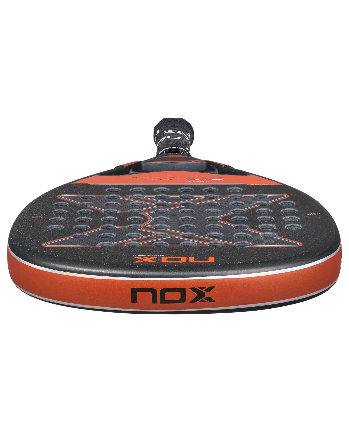 A close-up of the Nox AT10 Luxury GENIUS ATTACK 12K 2025 by Agustin Tapia from Padel USA shows a black, diamond-shaped racket with orange accents, circular holes, EXCLUSIVE SPIN tech, and the NOX logo on its 12K carbon frame.