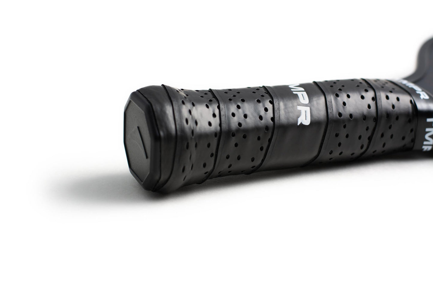 Close-up of the Expanse GXT by TMPR Sports: a black, perforated grip handle wrapped in textured tape. The end cap with a partially visible white logo and the widebody design stand out against a softly lit white background.