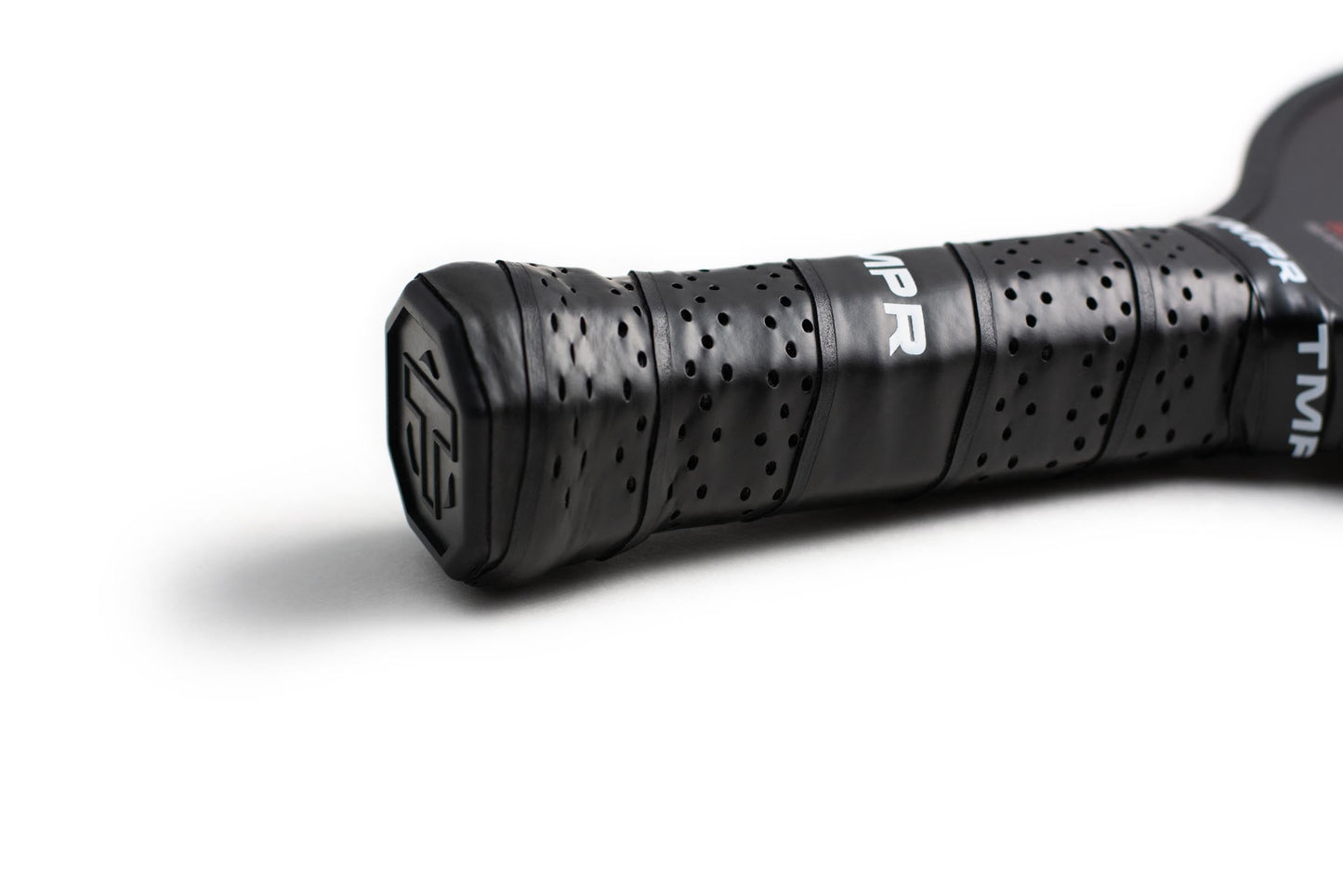 Close-up of a black, perforated Tantrum LX pickleball paddle grip by TMPR Sports. The grip is tightly wrapped for better performance, with TMPR lettering on the paddle’s face, shown against a clean white background.