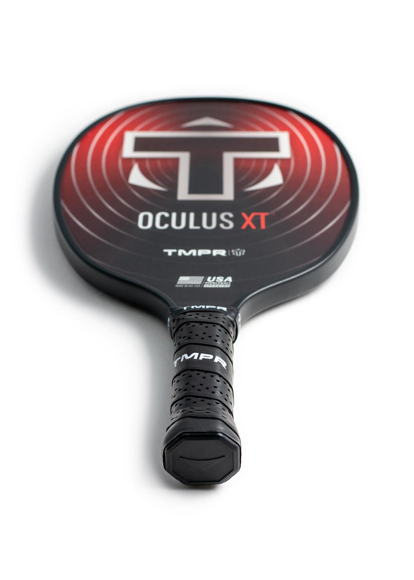 A black and red TMPR Sports Oculus XT paddle lies flat on a white surface, displaying concentric red circles, a large white T, "OCULUS XT," "TMPR," spin control features, USA Pickleball approval marks, and a black grip-taped handle.