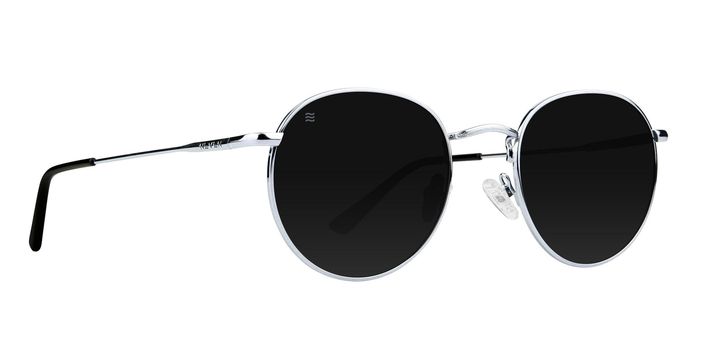 The Ivy by Neven Eyewear features round black lenses, thin stainless steel frames, black earpieces, and clear adjustable nose pads. This minimalist design delivers modern style and polarized UV400 protection against a white background.