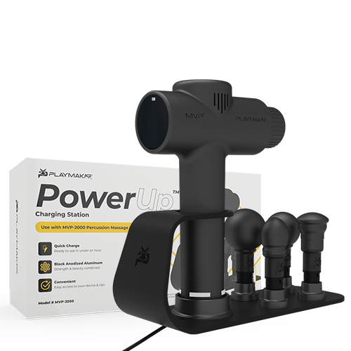 A black percussion massager with three interchangeable heads sits on a sleek MVP+ PowerUp Charging Station. Behind them, a white box labeled iReliev showcases product features and MVP+ PowerUp Charging Station branding.