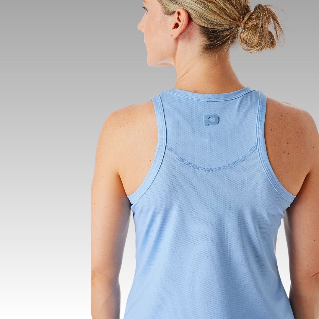 A woman with blonde hair in a low ponytail is shown from behind, wearing the Pretty Tank by Playly Store in light blue. The background features a smooth gradient from gray at the top to white at the bottom.