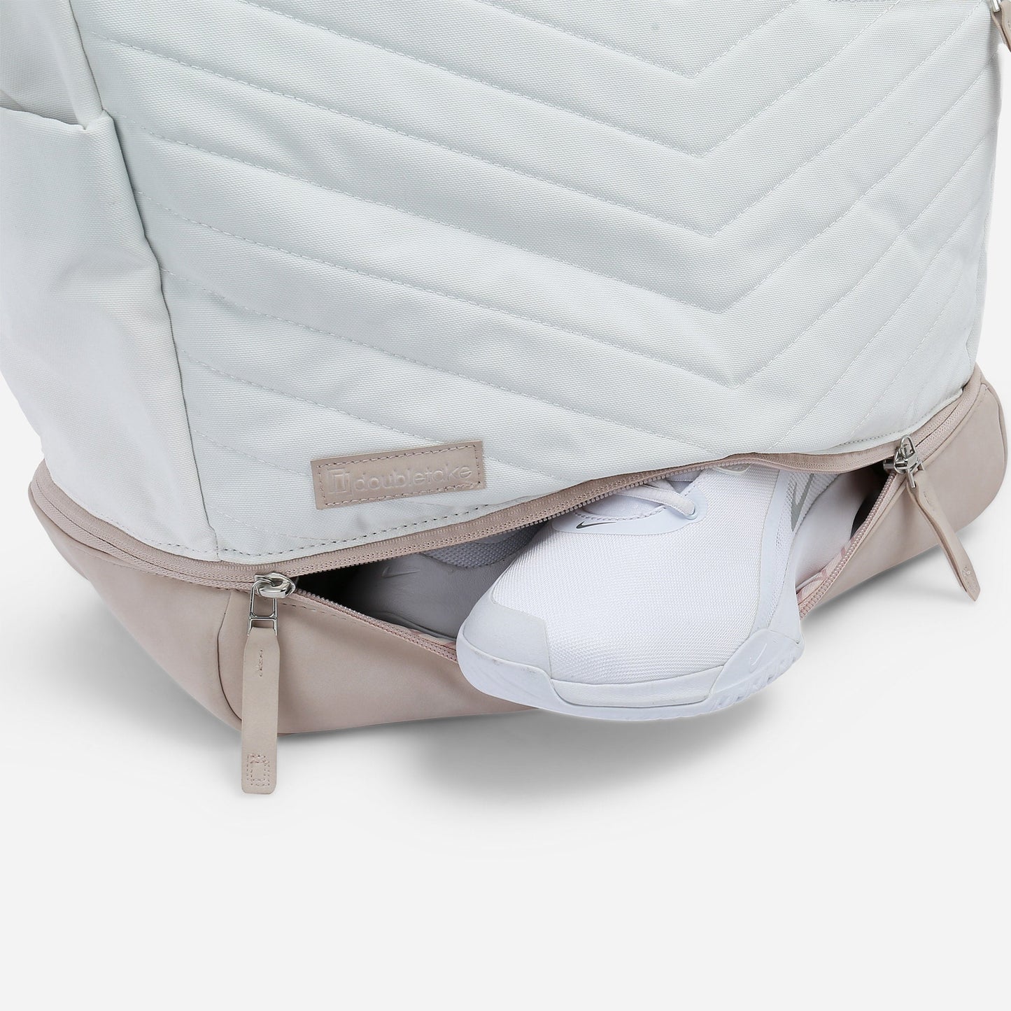 A white and beige PARISII | Pickleball Tote by Doubletake is shown with a quilted pattern. The front bottom compartment is open, revealing white sneakers. The hybrid design features a stitched Doubletake label.