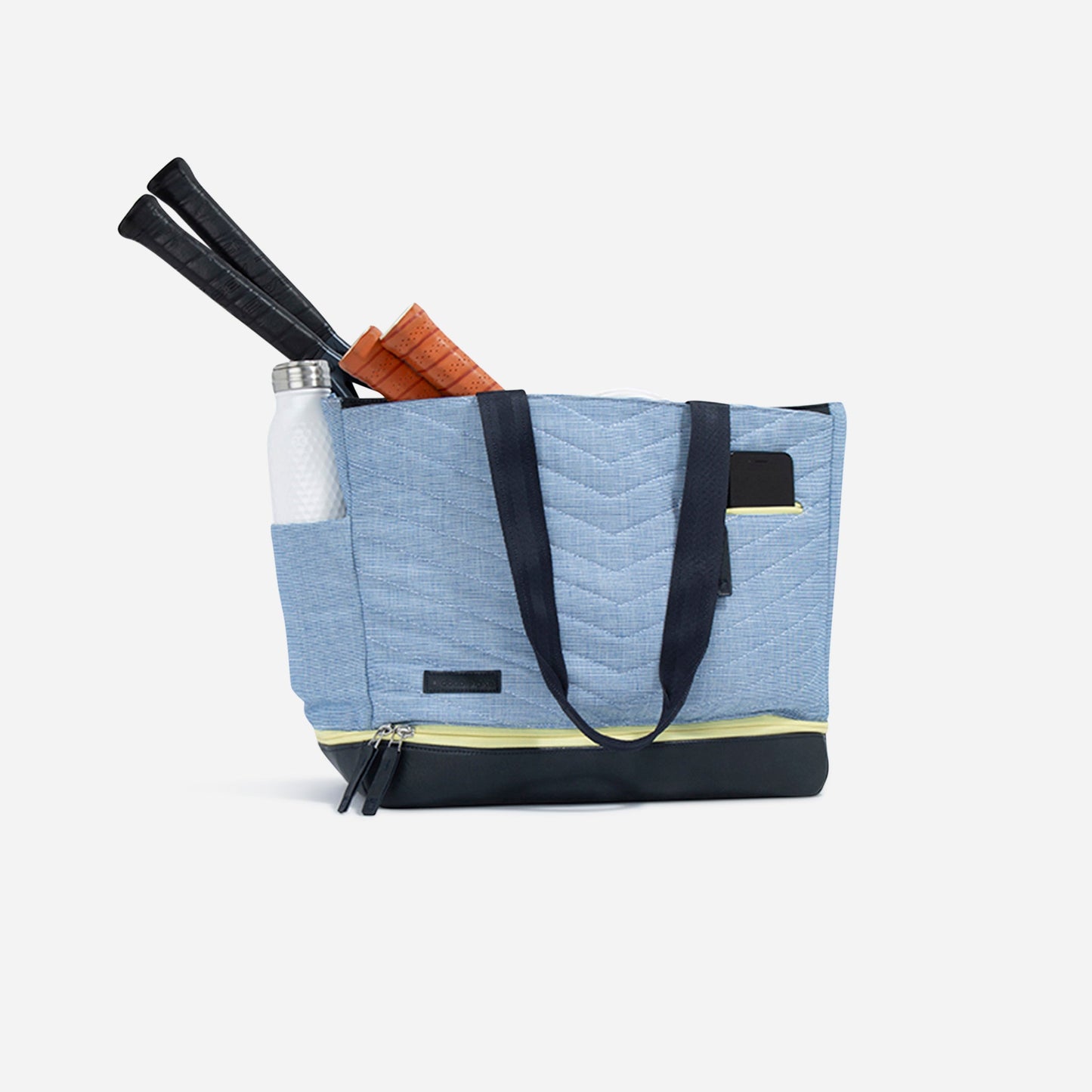 The Doubletake PARISII Pickleball Tote is a light blue quilted bag with black handles and base, front phone pocket, side pocket with a white water bottle, and two racquet handles visible. The tote is set against a plain white background.
